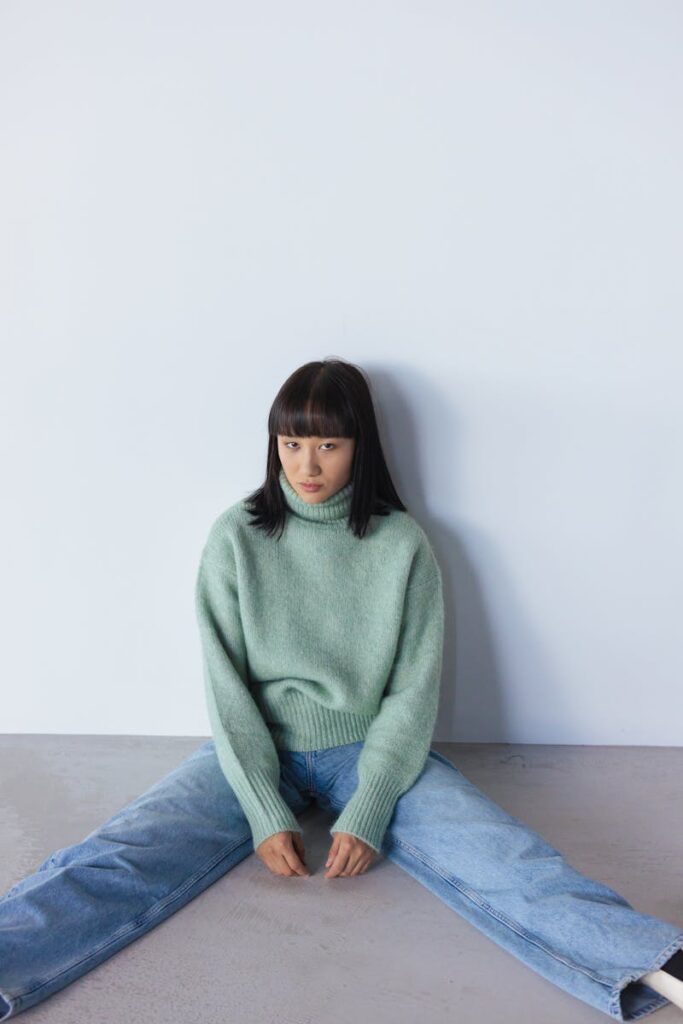 Model in turtleneck and jeans sitting on floor, modern fashion look.