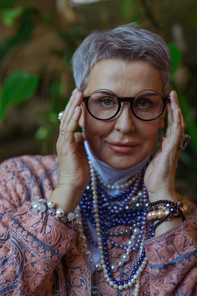 Portrait of a stylish senior woman wearing jewelry and eyeglasses, expressing joy with a warm smile.