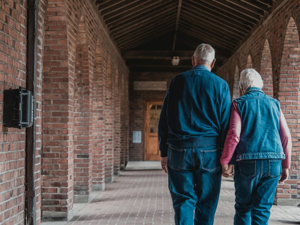 An elderly couple holding hands as they walk through a brick corridor, exuding love and companionship.
