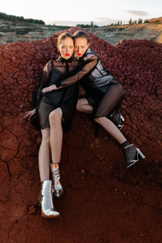 Two models in stylish dresses and boots posing on red rock terrain.