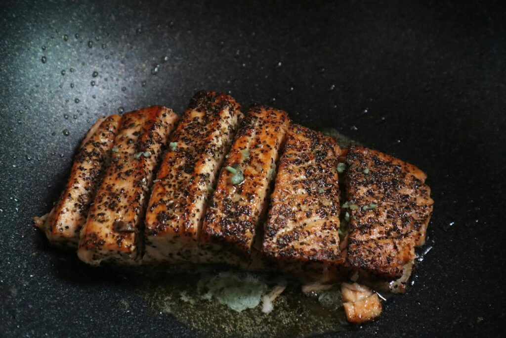 Sizzling grilled salmon steaks with herbs in a non-stick frying pan for a savory meal.