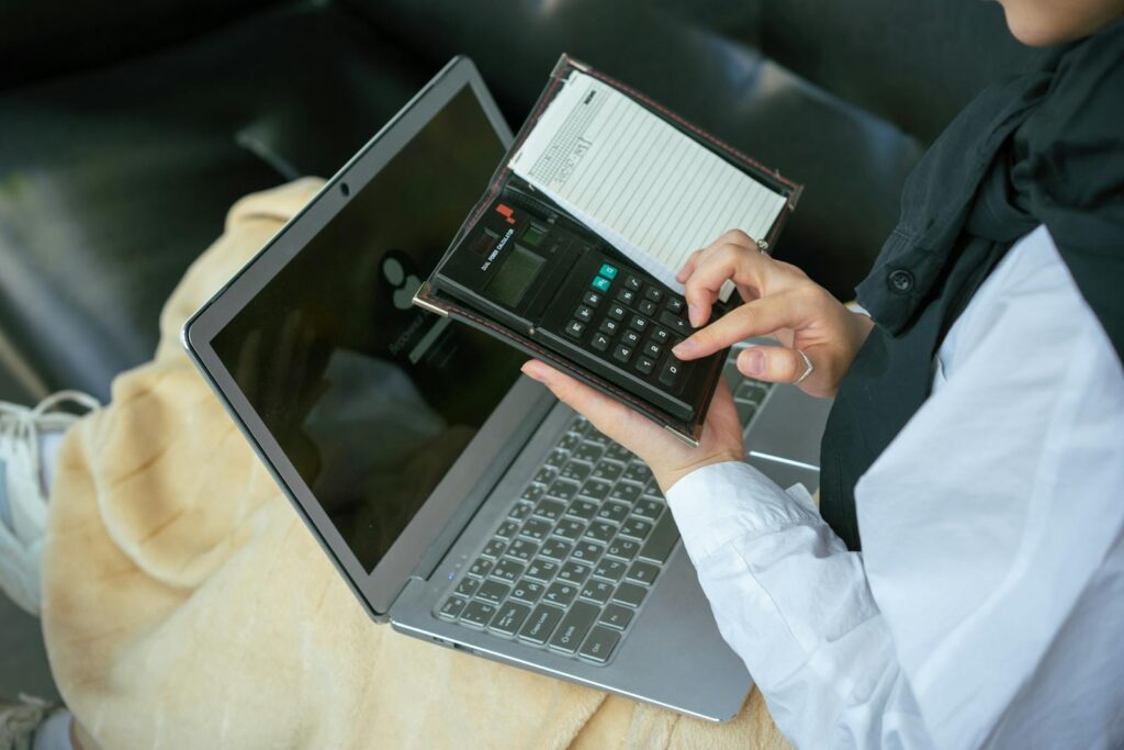 Close-up of a person using a calculator with a laptop, symbolizing home office productivity.