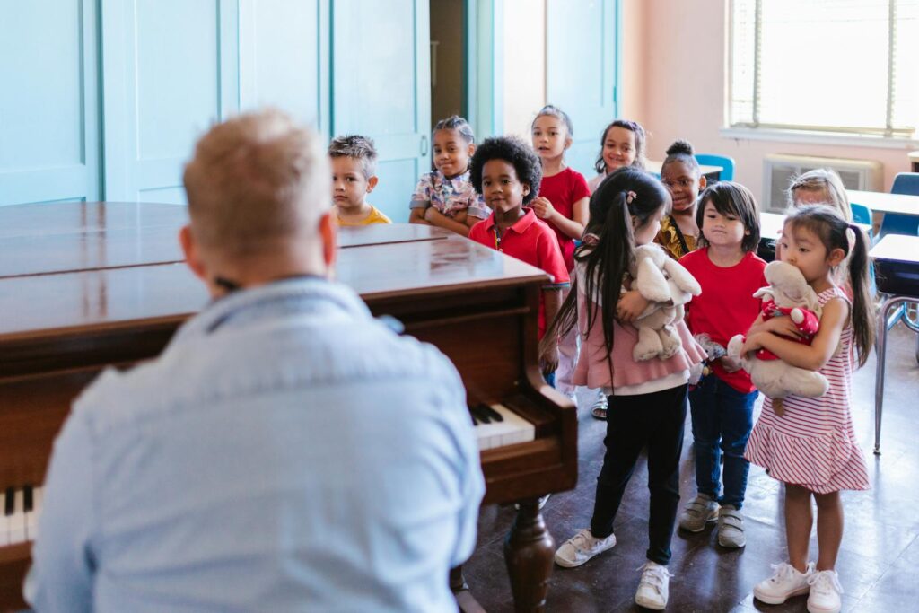 A group of children participate in a lively music class led by a teacher in an indoor school setting.