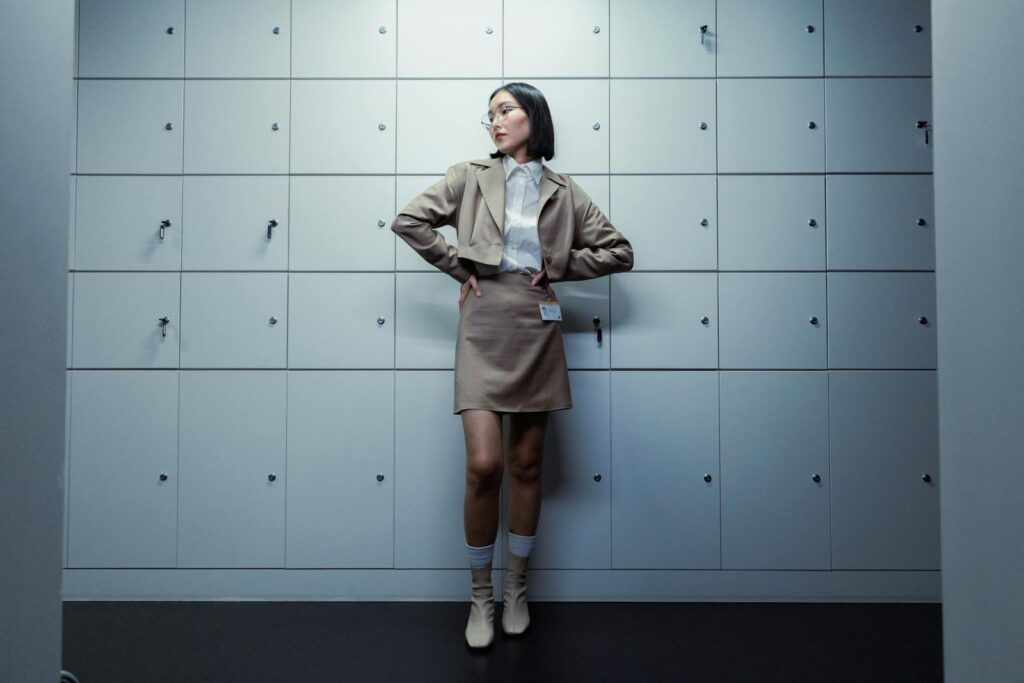 Confident woman in a blazer and skirt posing in front of office lockers, looking aside.
