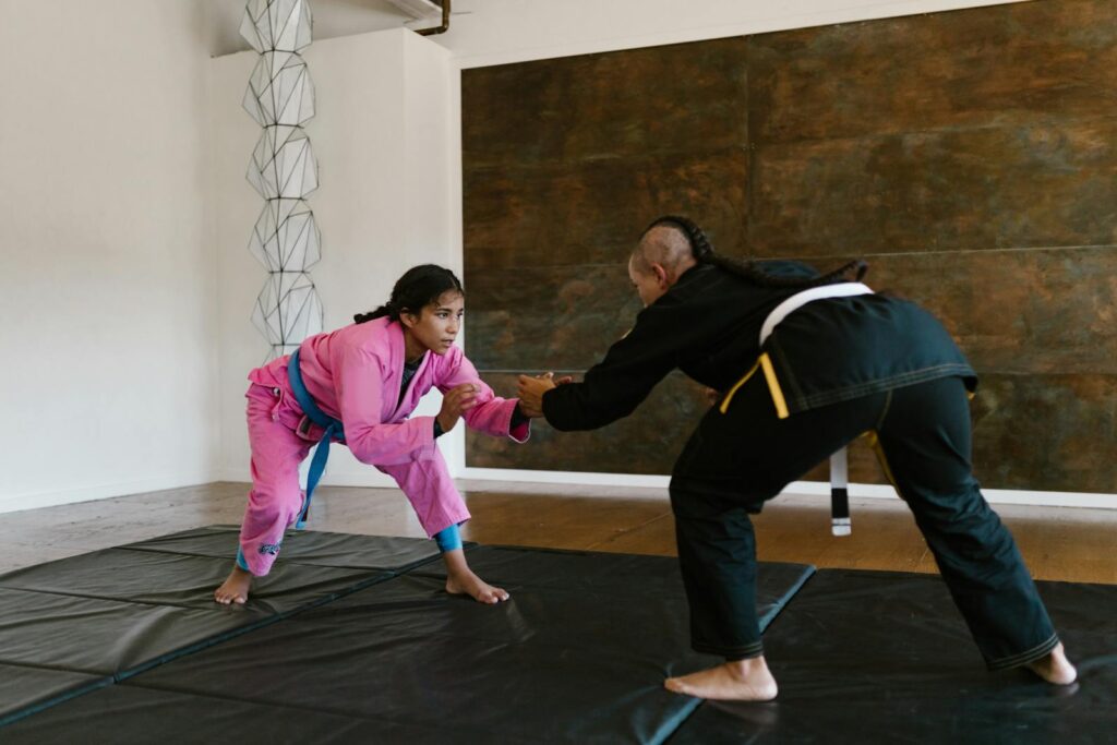 Two women engaged in martial arts practice indoors, highlighting strength and technique.