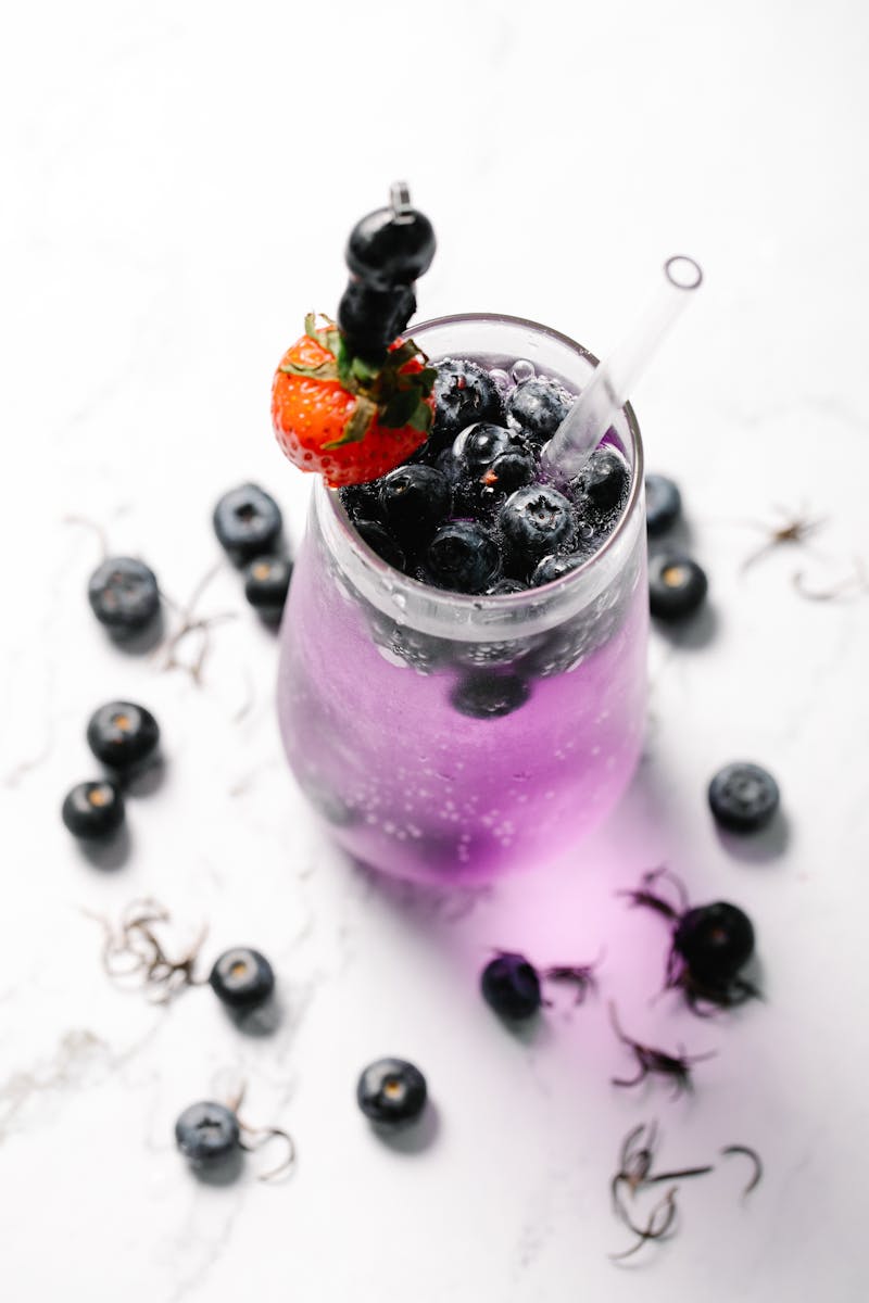 A glass of vibrant blueberry cocktail garnished with fresh strawberries and scattered berries.