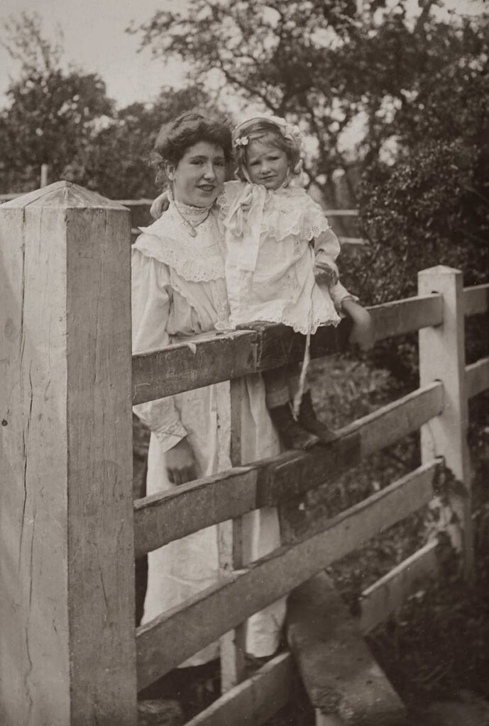 Classic vintage photo of a mother and daughter posing by a wooden fence in a natural setting.