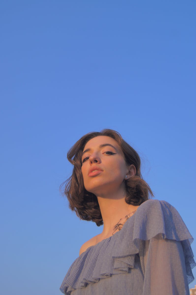 Portrait of a woman in a blue off-shoulder top against a clear sky.