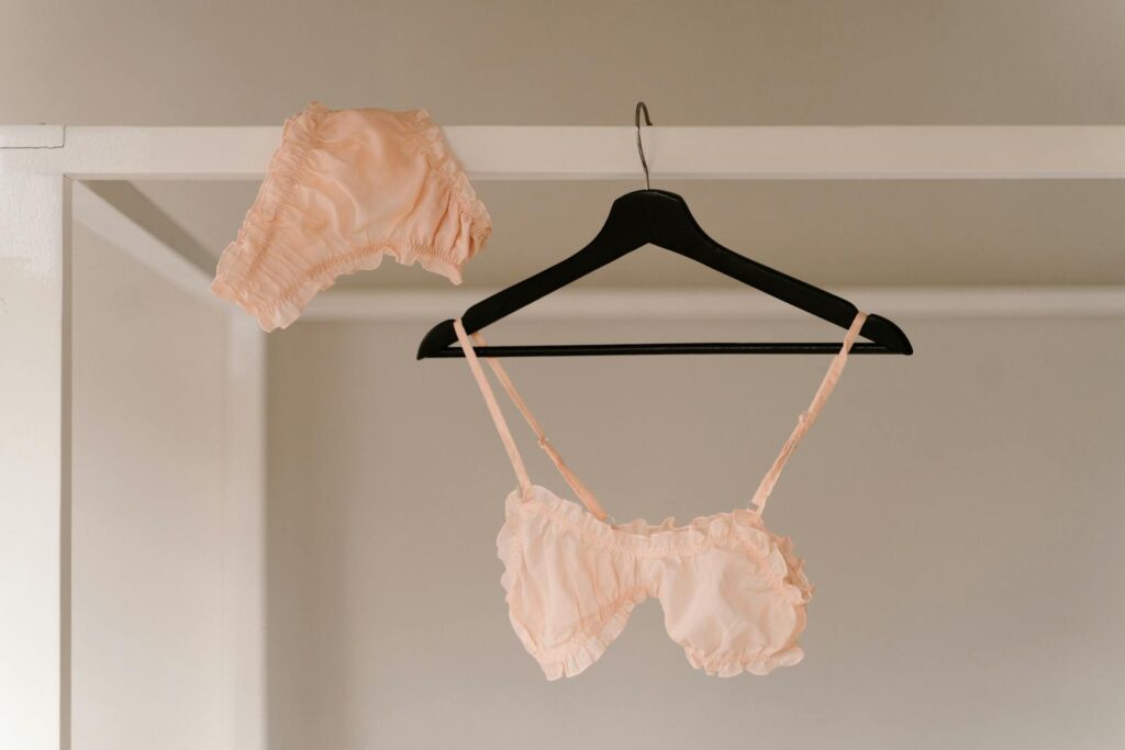 A soft pink lingerie set displayed on a clothes hanger indoors, showcasing intimate fashion.