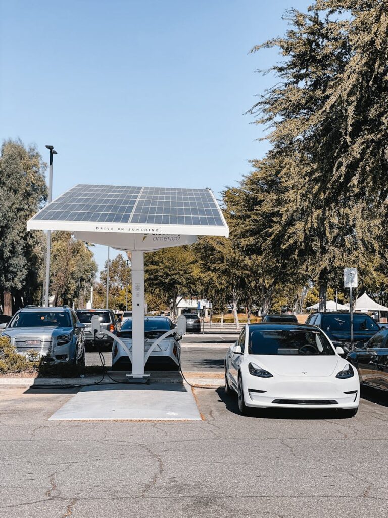A white electric car charging under a solar panel in an urban setting, showcasing renewable energy use.