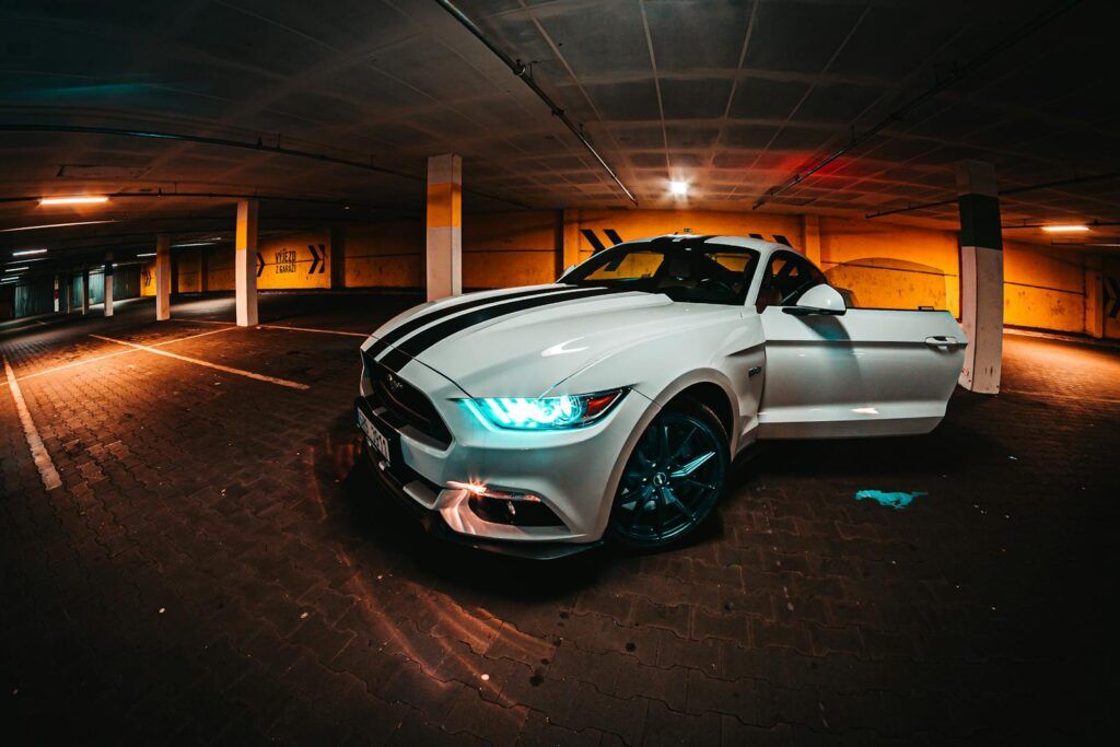 A striking white sports car with headlights on parked in an urban parking garage at night.