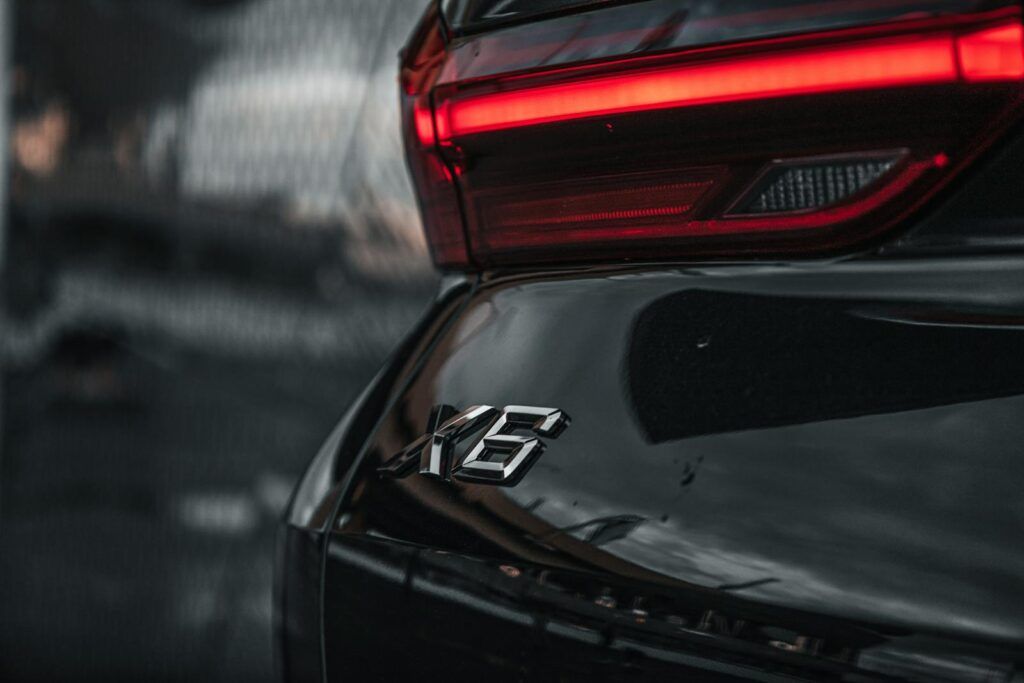 Artistic close-up of a car's rear showcasing taillight and 'X6' emblem in moody lighting.