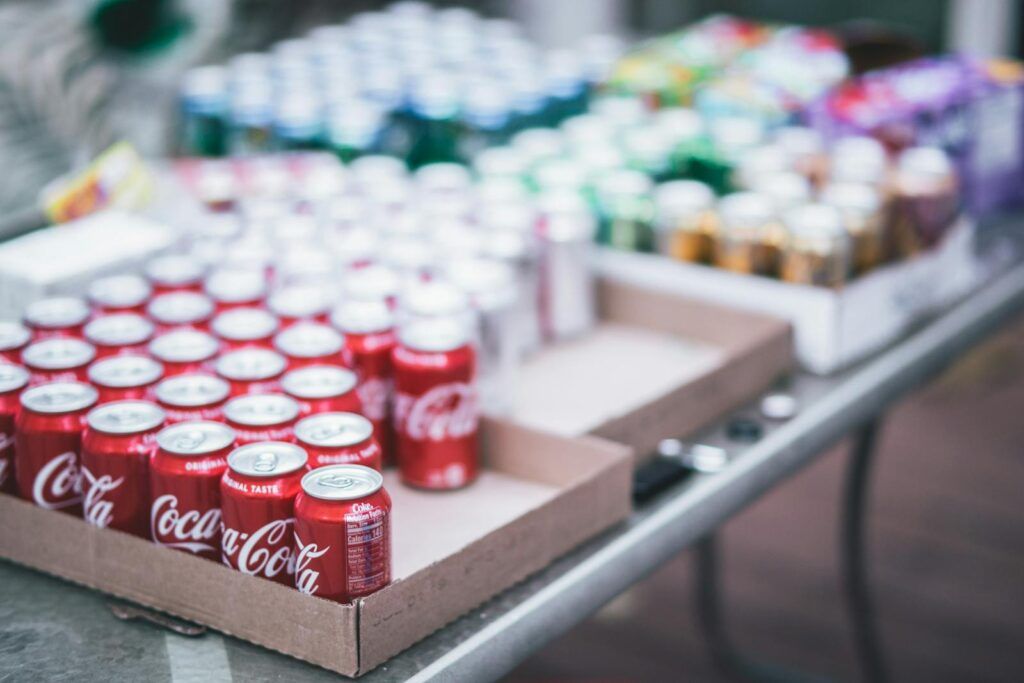 Blurred image of assorted beverage cans on a table, featuring Coca-Cola.