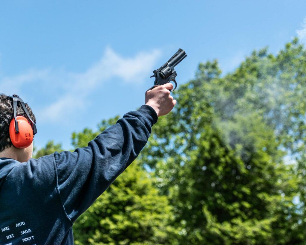 Close-up of a person firing a starting pistol outdoors with blue sky