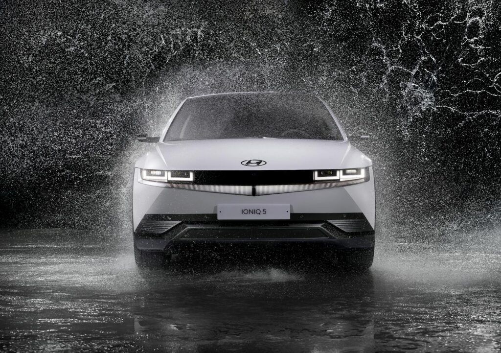 Dynamic front view of a Hyundai Ioniq 5 splashing through rain, captured in black and white.