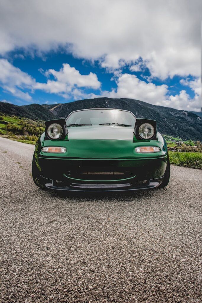 Front view of a green Mazda MX-5 sports car on a rural road with mountainous backdrop.