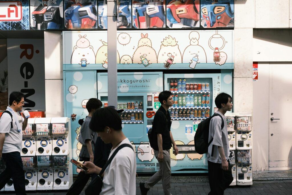 Pedestrians walk past colorful vending machines with cartoon graphics in an urban setting.