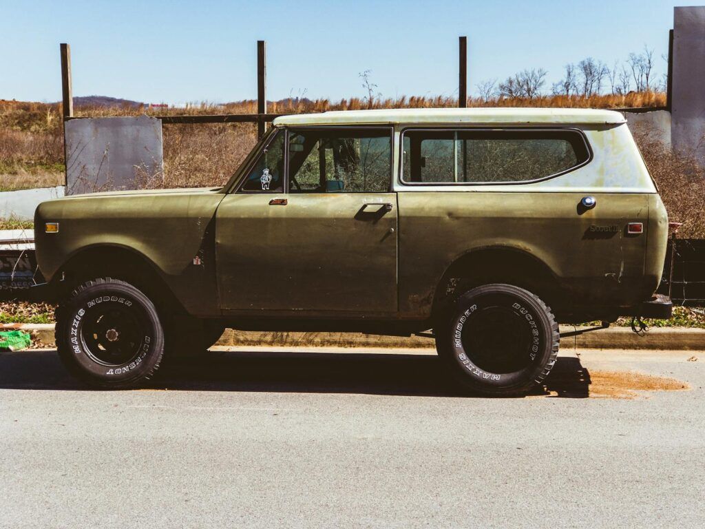 Rustic classic SUV parked on an empty road with a clear blue sky in the background.