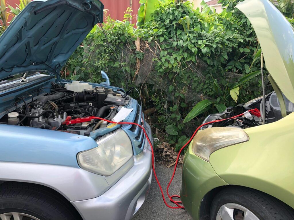 Two cars connected by jumper cables in a parking lot for a battery charge.