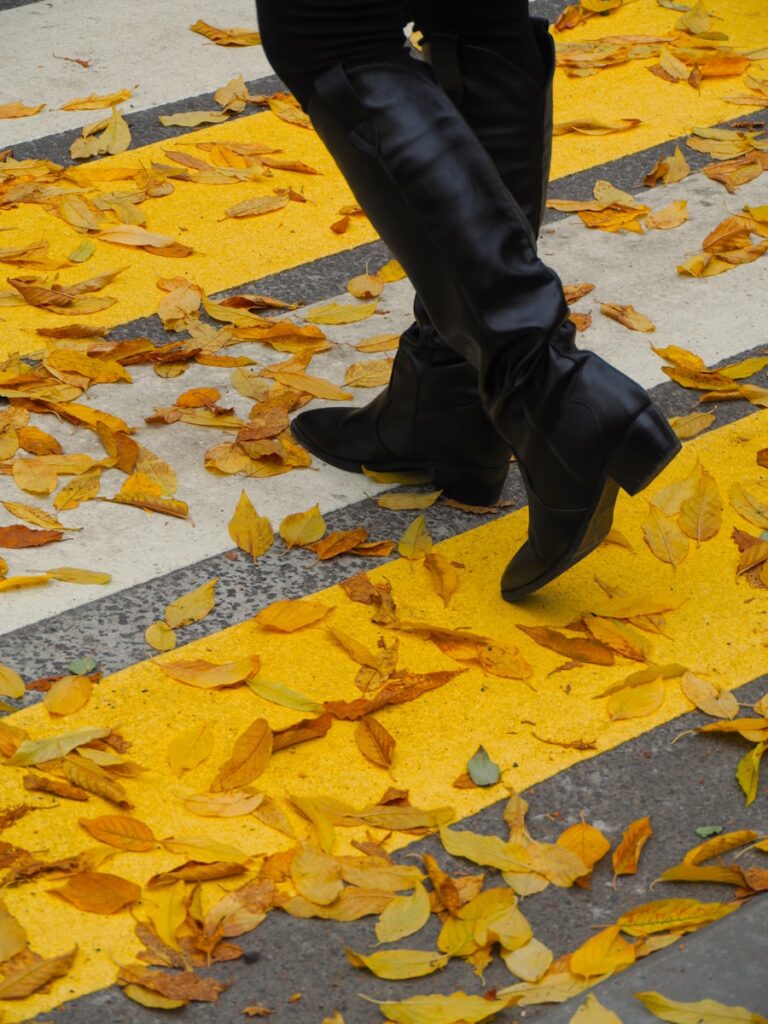 A woman walking down a street next to yellow leaves
