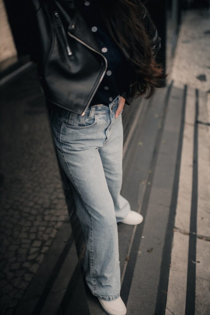 Woman in jeans and jacket standing outside.