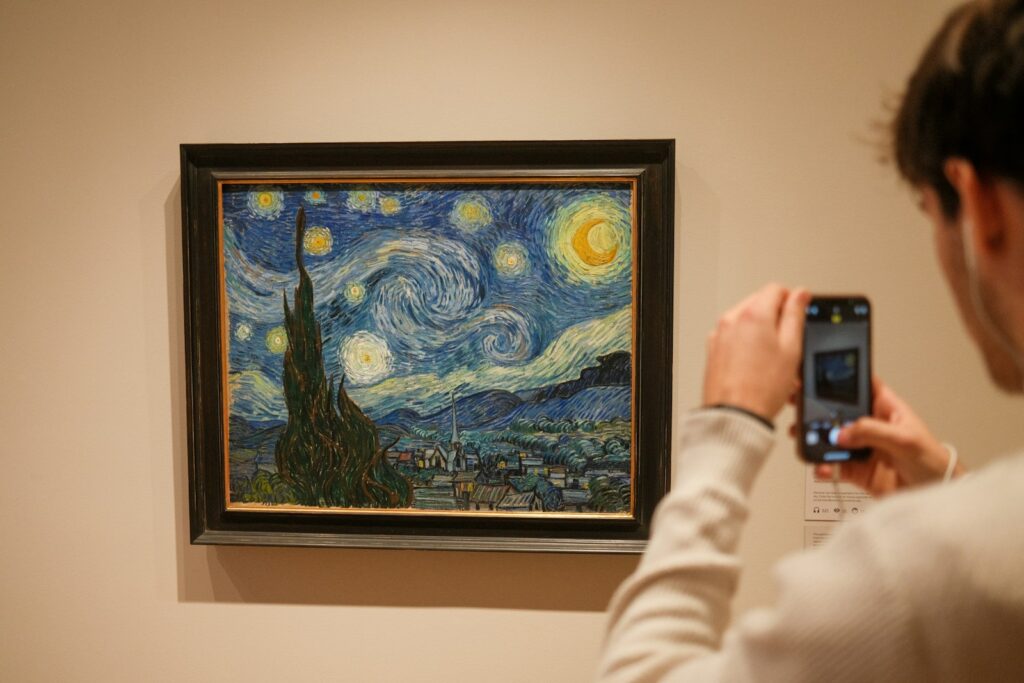 a woman taking a picture of a painting with a cell phone