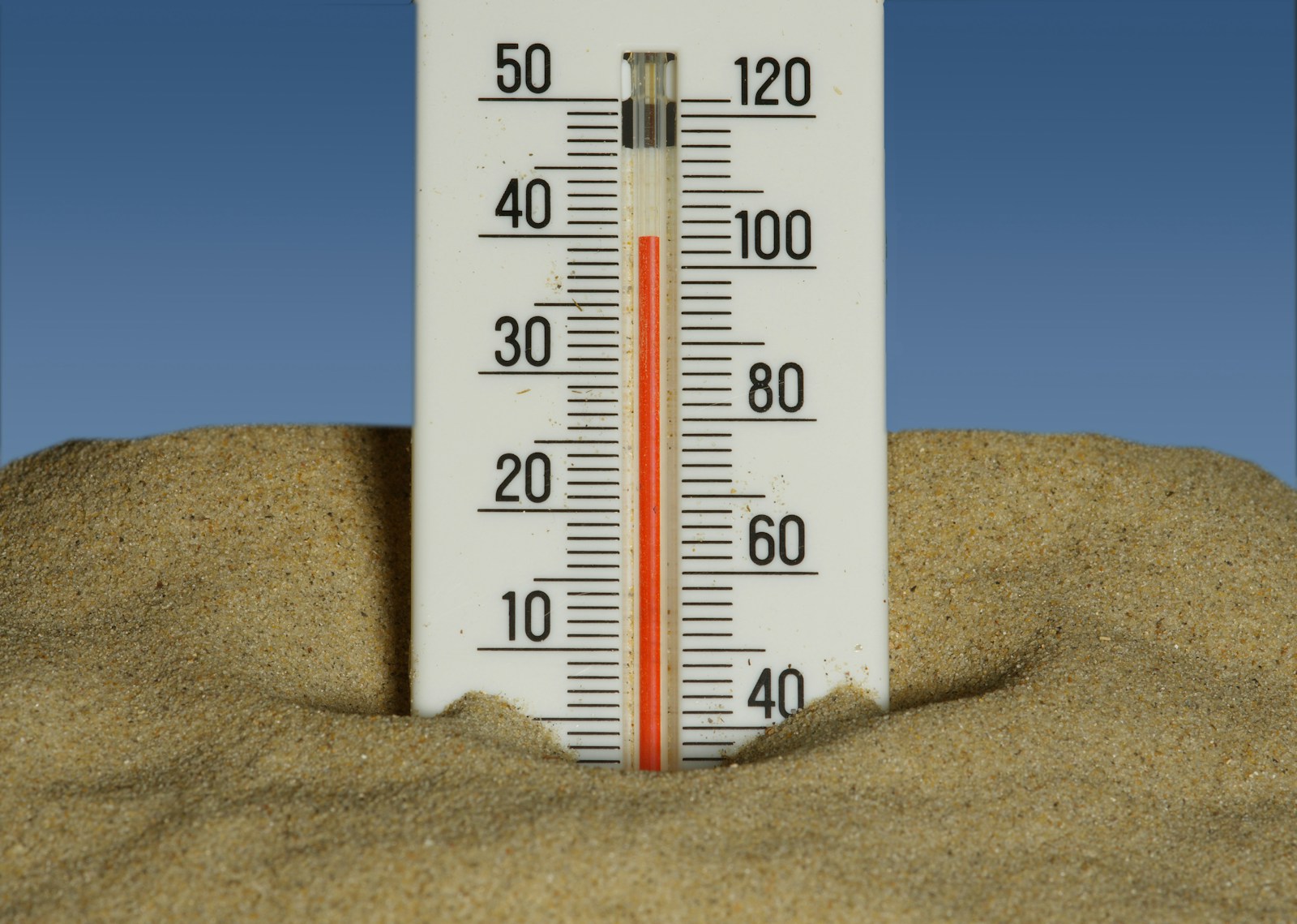 A thermometer in the sand with a blue sky in the background