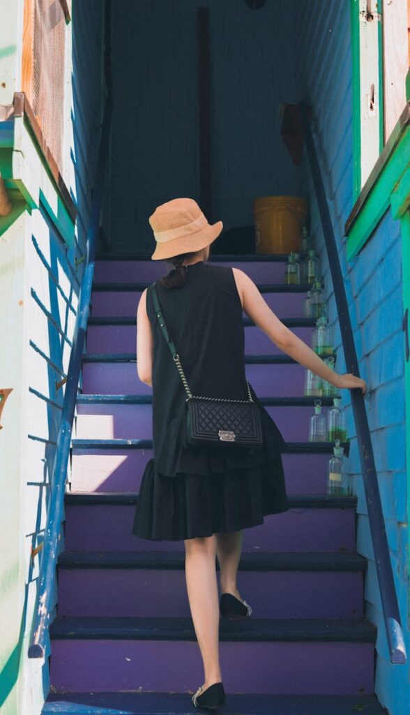 woman in black dress wearing brown hat standing on blue staircase