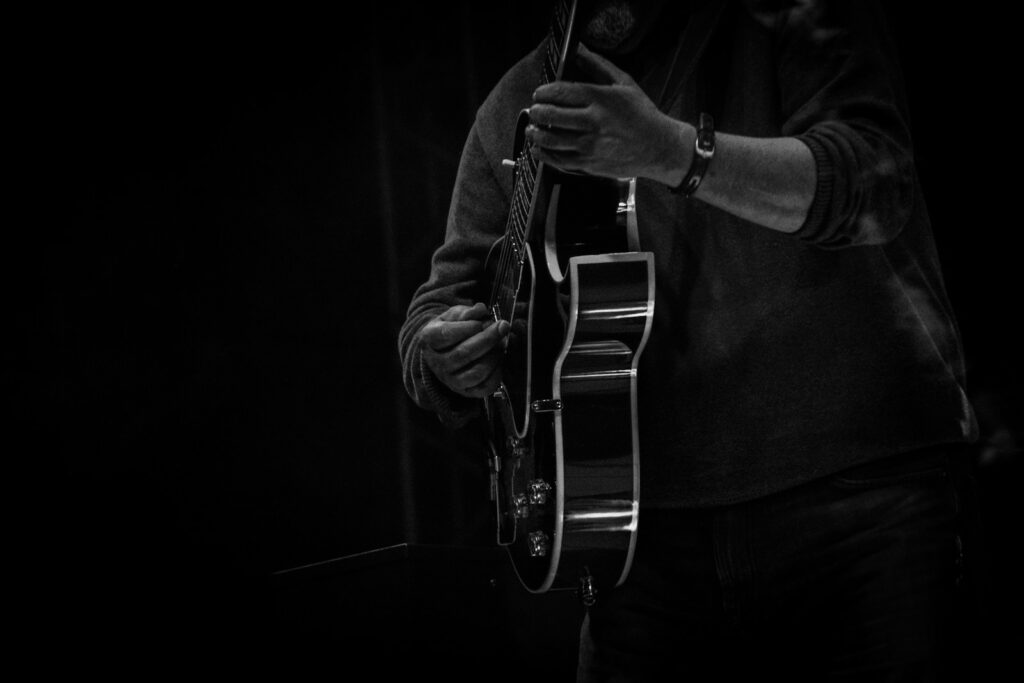 man playing guitar in grayscale photography