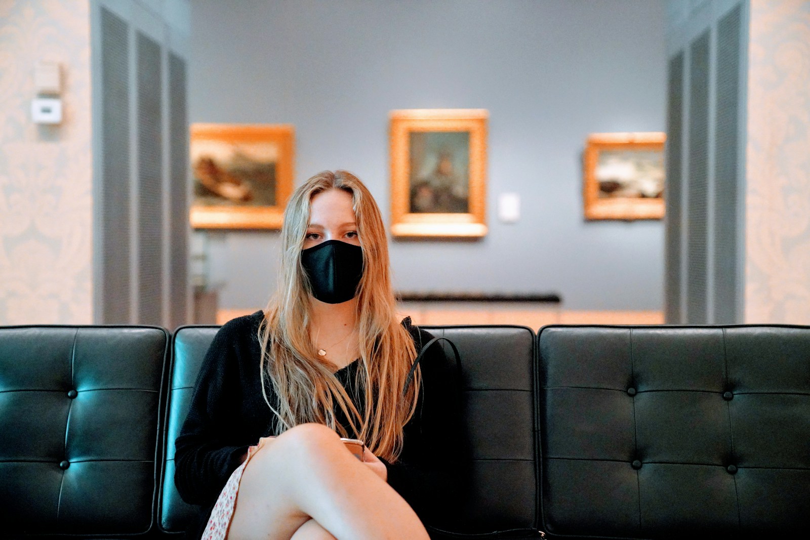 a woman sitting on a couch with a black mask on her face