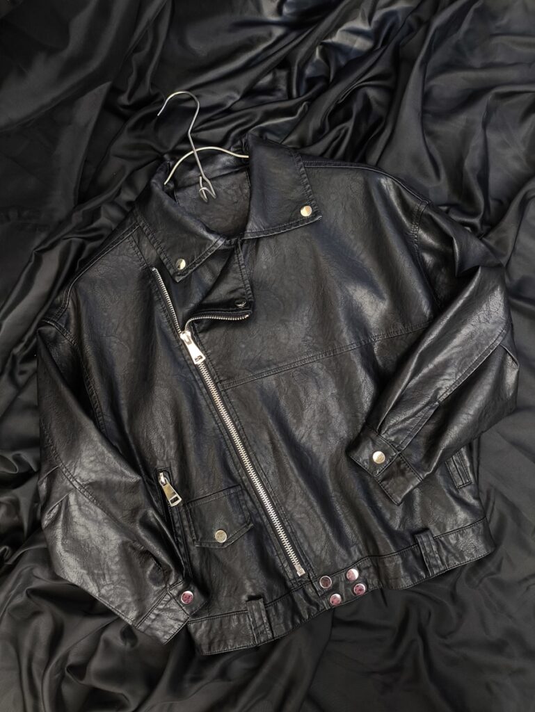 A black leather jacket laying on top of a bed