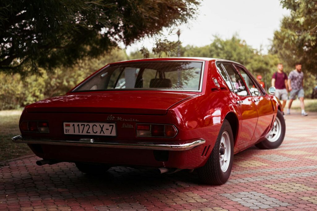 Rear view of a classic red Iso Rivolta sedan parked outdoors on a tiled path.