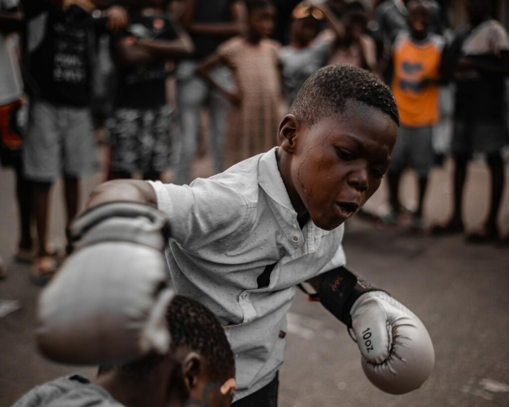 A young boy passionately engaged in a boxing match outdoors, showing determination.