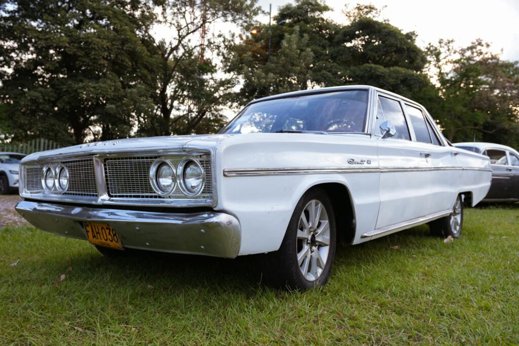 Vintage white Dodge Coronet parked on a grassy field during the day.