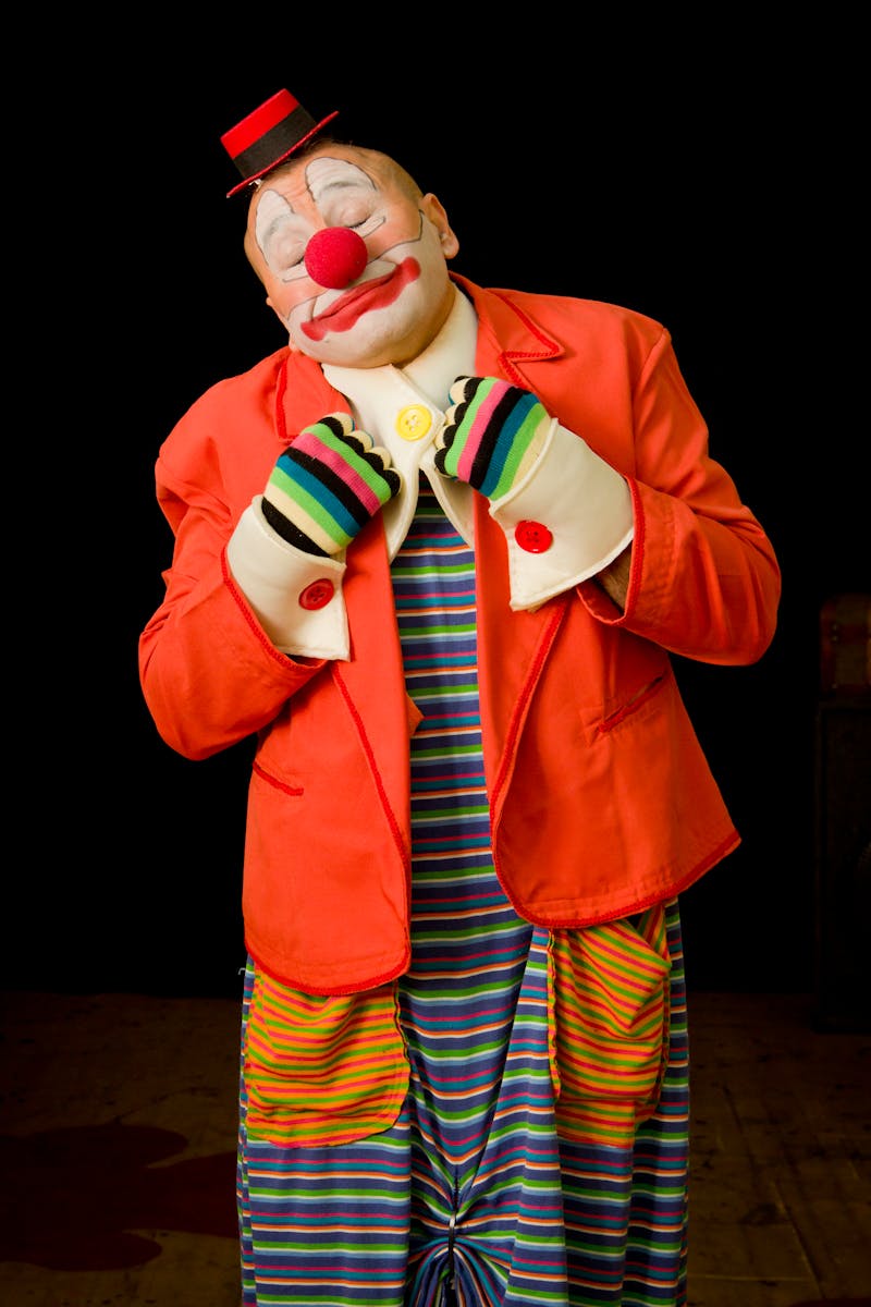 Vibrant clown in red jacket on stage, embodying humor and performance art.