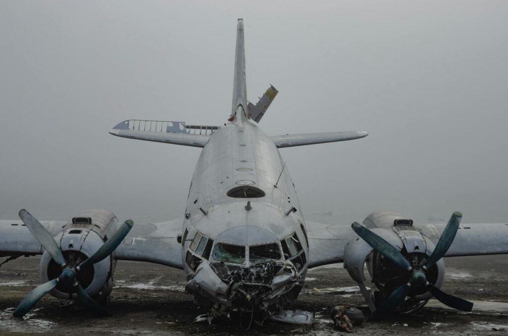 A derelict aircraft with damaged propellers on a foggy tarmac, conveying a sense of decay.