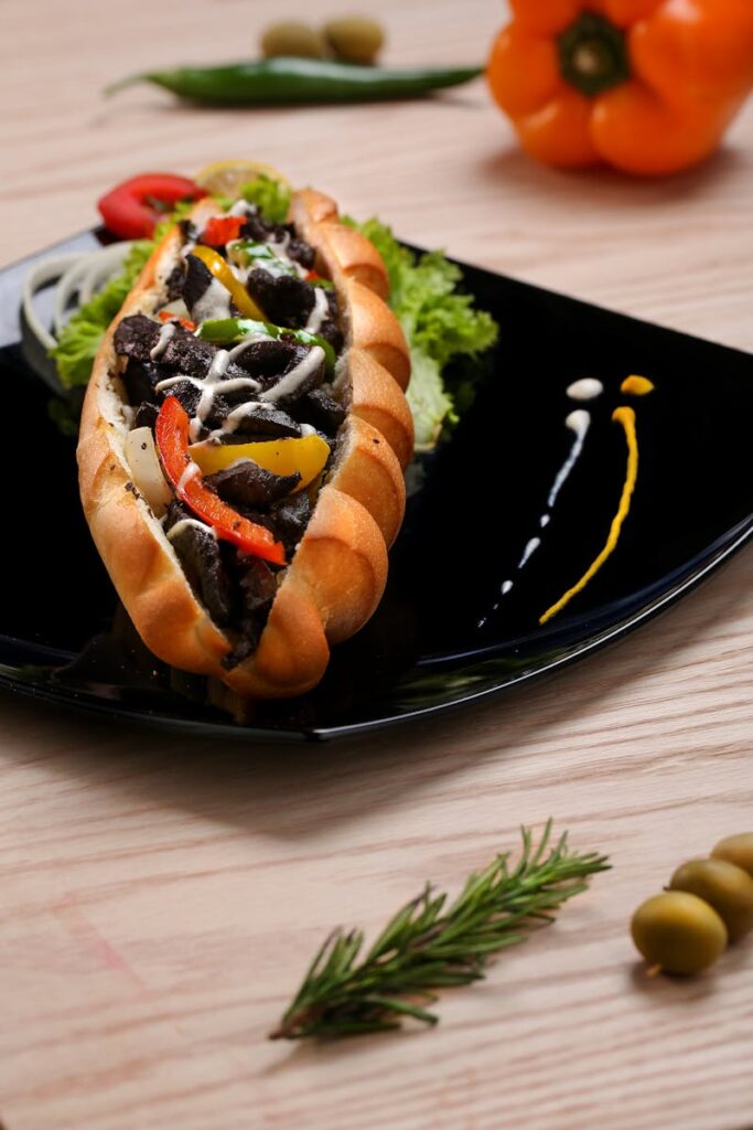 Delicious beef sandwich with peppers and greens served on an elegant black plate.