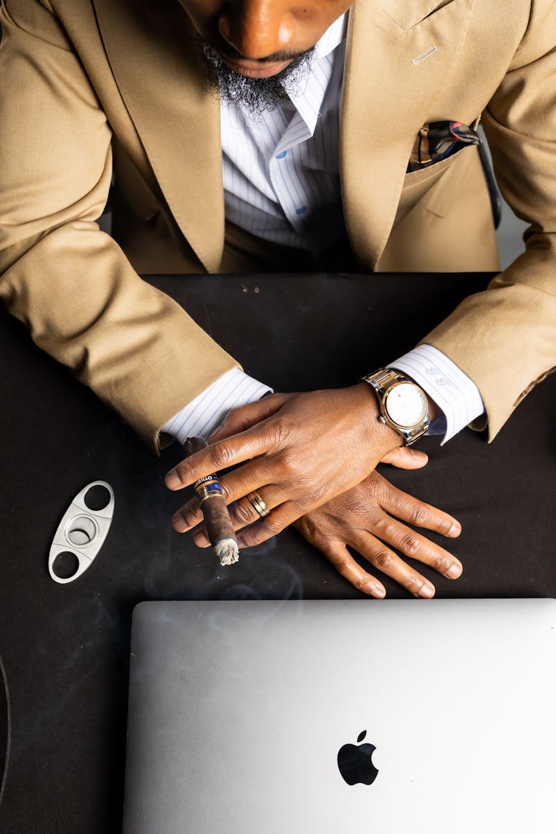 Sophisticated adult in suit with cigar, beside laptop. Stylish and composed.