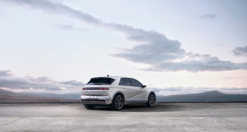 A sleek white electric SUV parked on an open road with a scenic backdrop of mountains and sky.