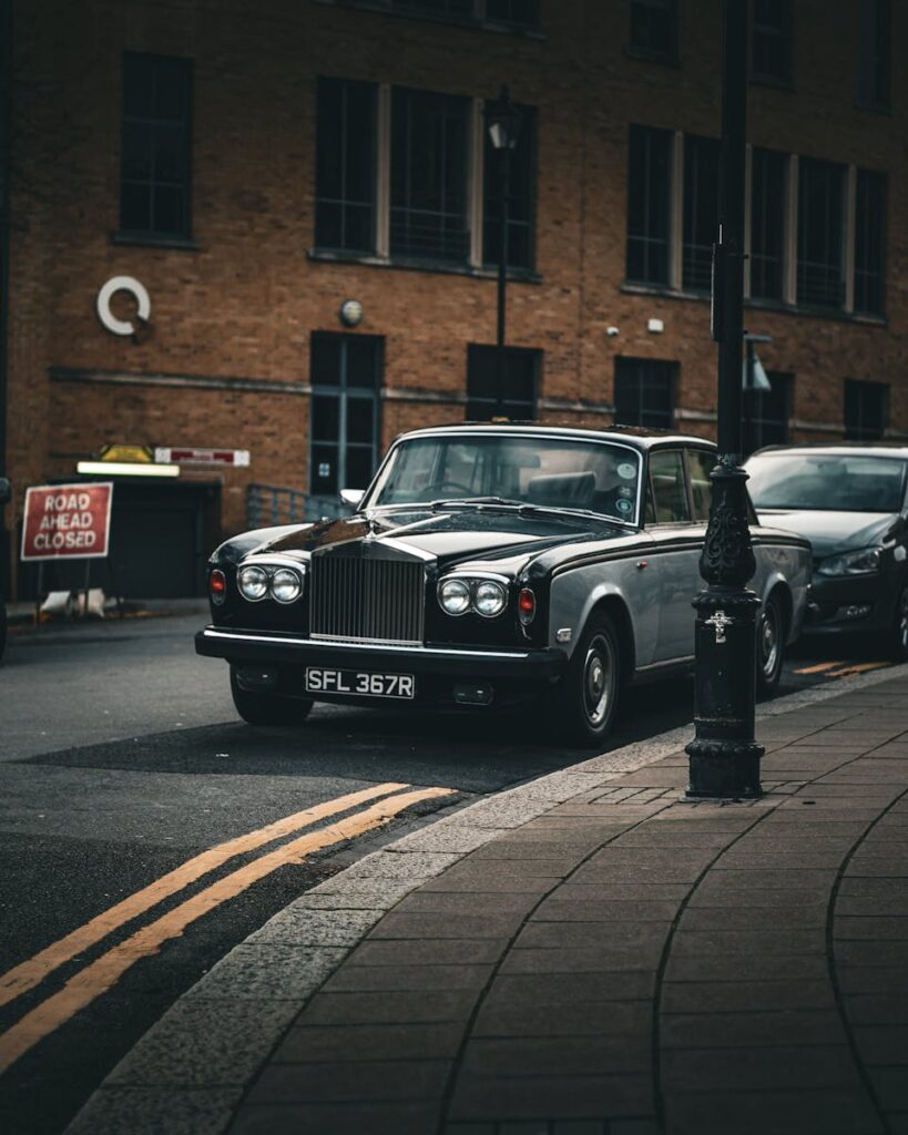 Classic Rolls-Royce parked on urban street with closed road sign, evoking a vintage feel.