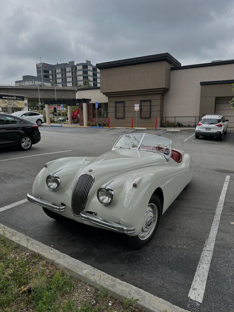 Classic Jaguar XK120 cabriolet parked in urban setting, showcasing vintage design and elegance.