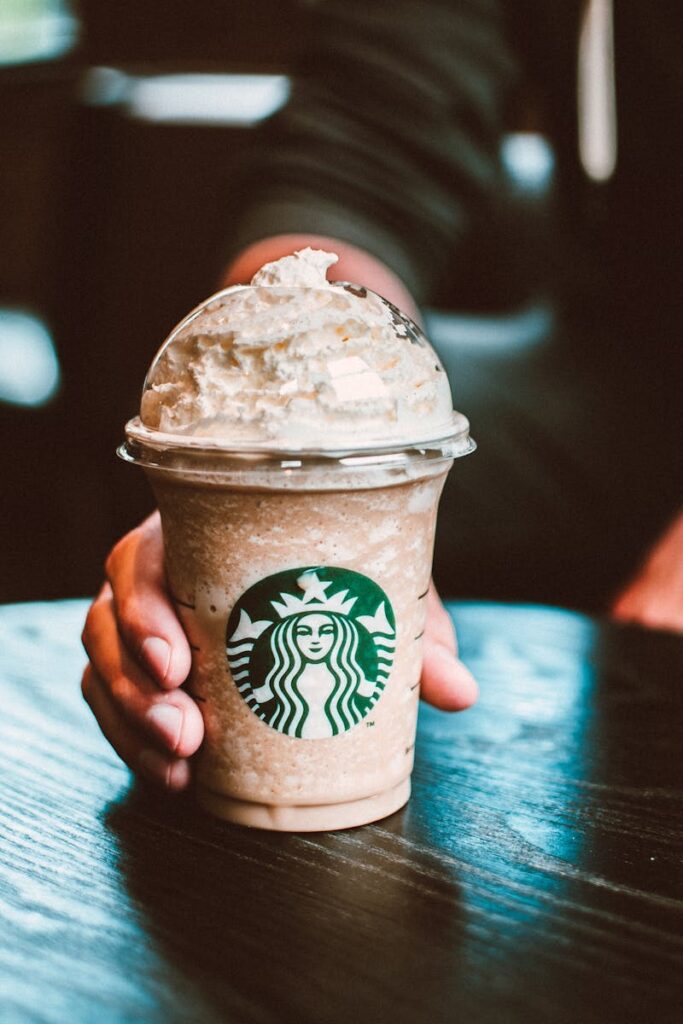 Close-up of a hand holding a Starbucks frappe on a dark wooden table indoors.