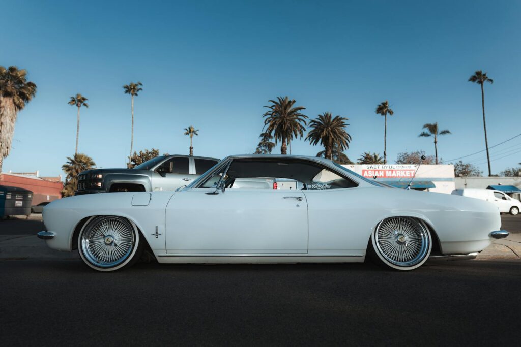 Classic white Chevrolet Corvair parked amidst palm trees with clear blue sky.