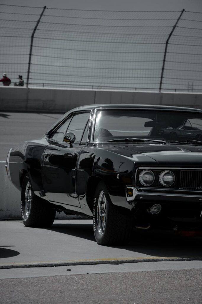 Vintage black Dodge Charger parked at a racetrack under sunny sky, ready for action.