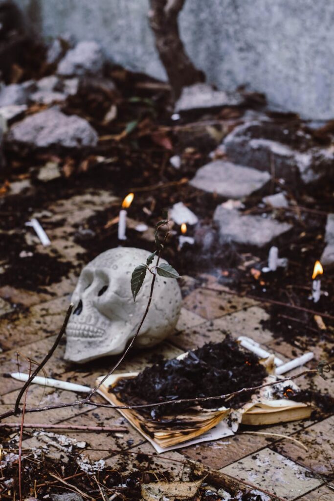 A spooky setup with a skull, burnt book, and candles for a Halloween vibe.