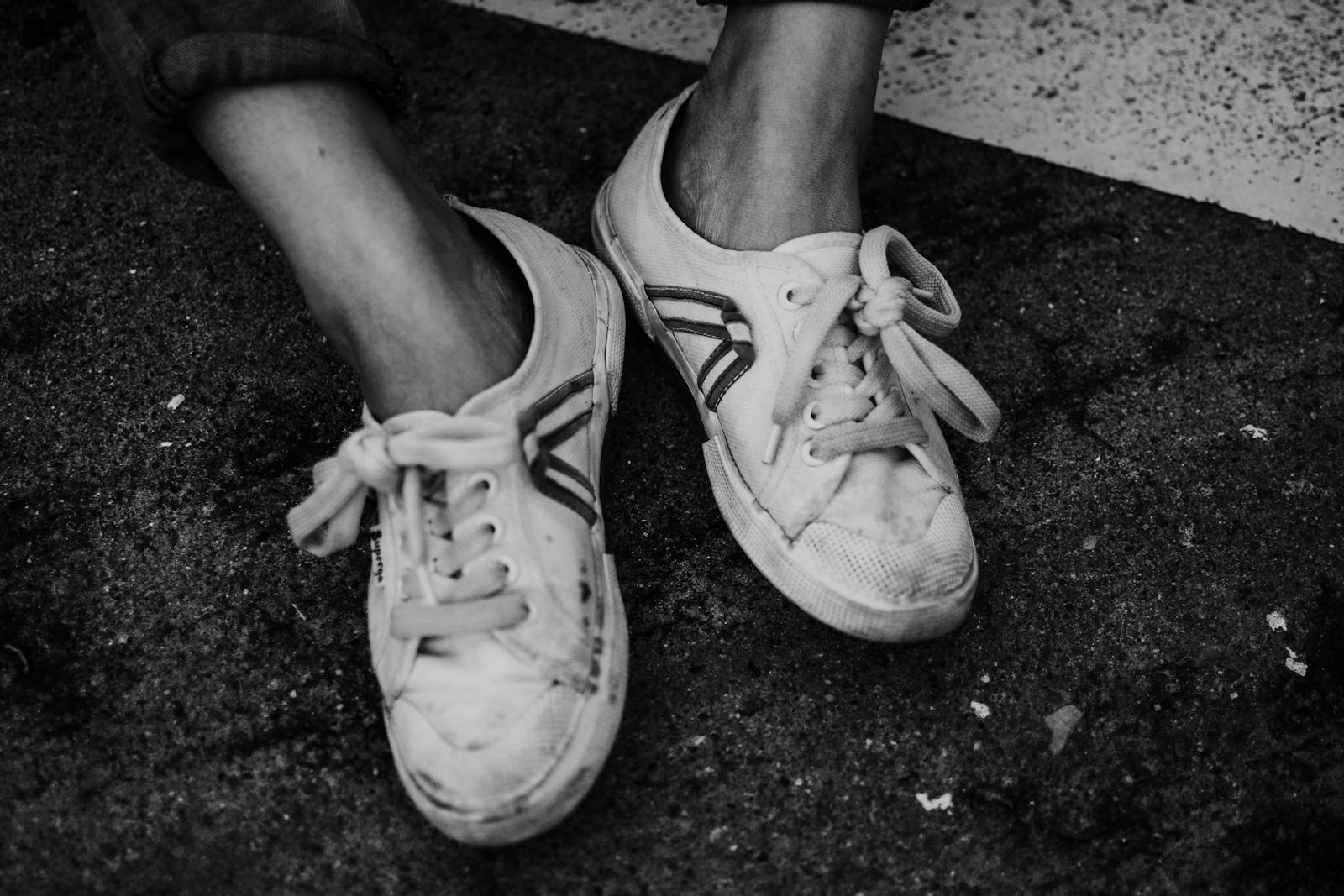 Black and white image of worn sneakers and feet on an urban pavement, highlighting street style.