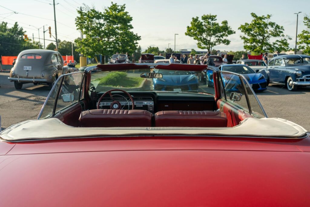 Rear view of a classic red convertible at a lively outdoor car show.