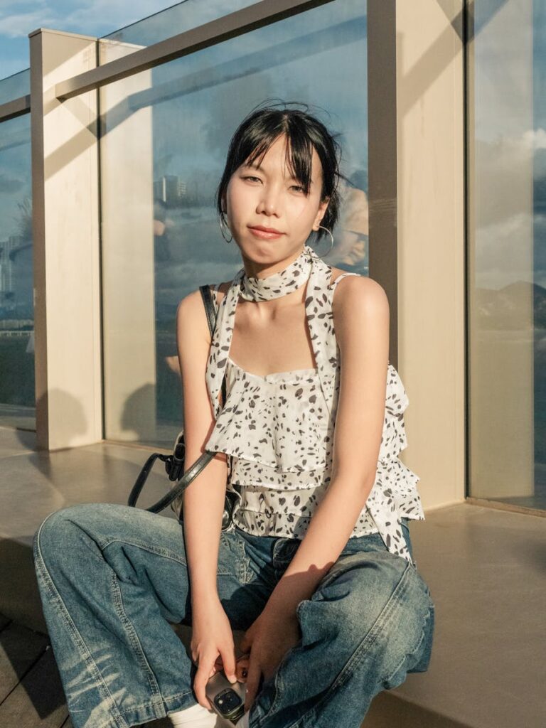 Young woman sitting outdoors in Shenzhen, wearing casual denim and floral top.