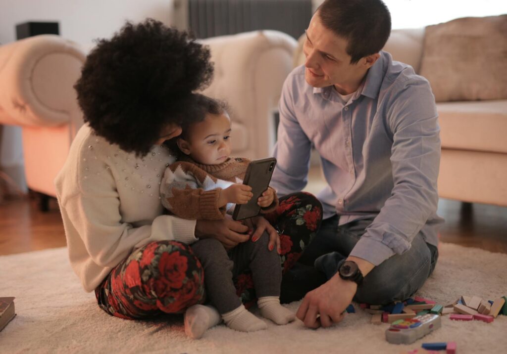 A family bonding with their toddler using a smartphone in a cozy living room setting.