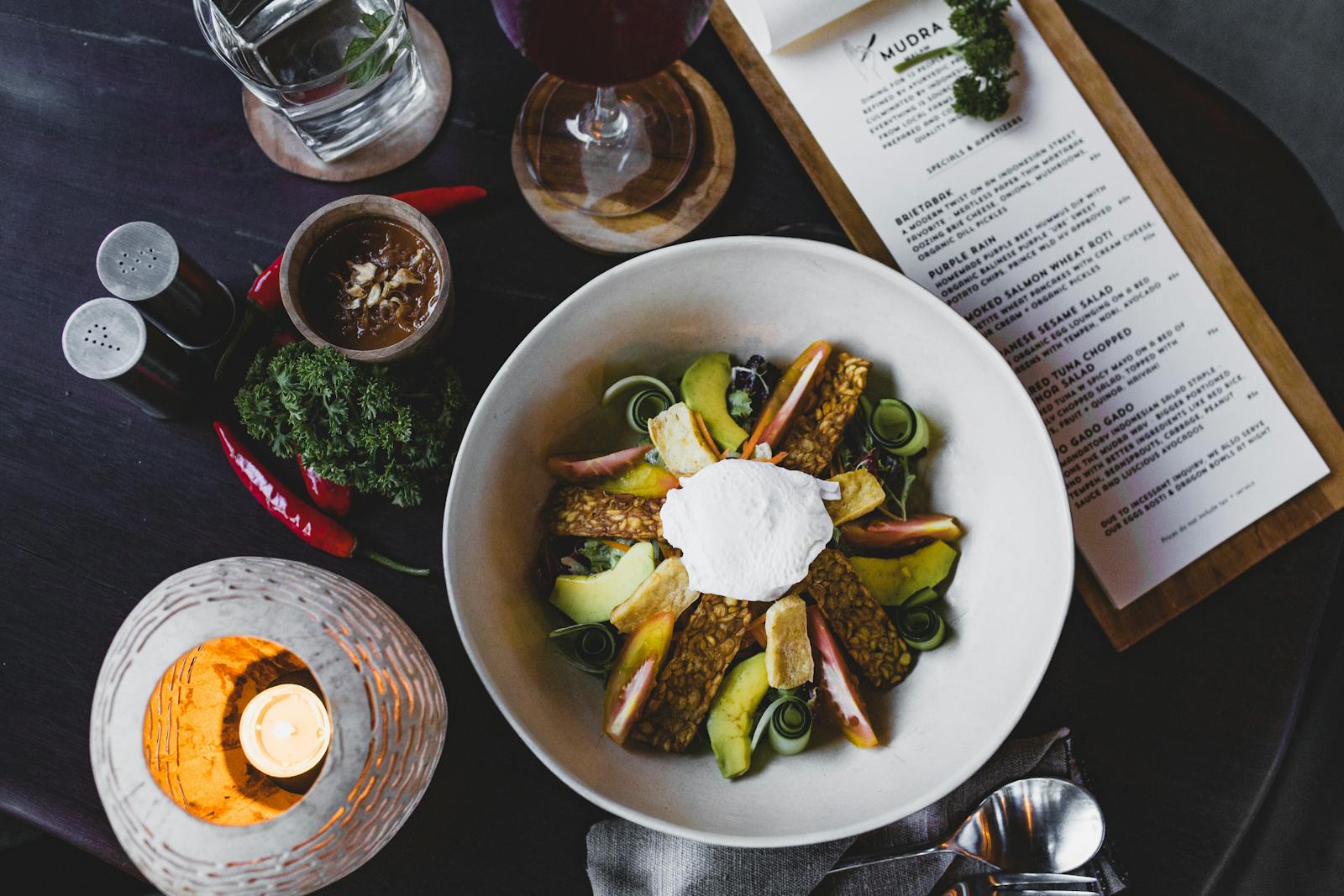 Top view of a gourmet vegan dish featuring avocado, tempeh, and vegetables on a restaurant table setting.